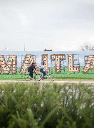 Couple riding their bicycles past the Welcome to Maitland Sign on Elgin St, Maitland