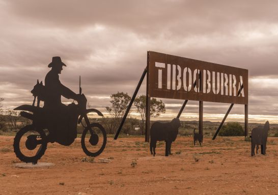 A sign and statues of sheep and a farmer on a motorbike welcome visitors to Tibooburra