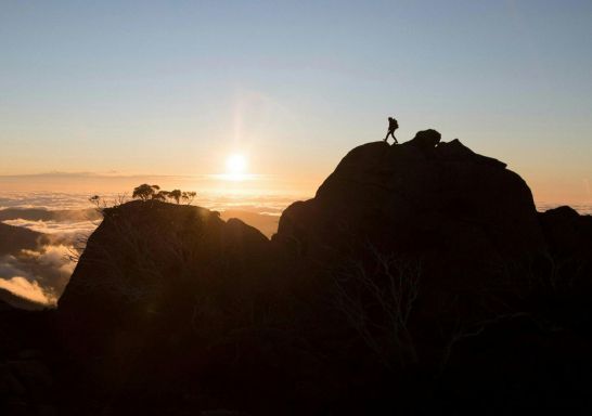 Hiker enjoying a scenic sun set from the top of a mountain at Kosciuszko National Park, Kosciuszko - Credit: Tourism Snowy Mountains