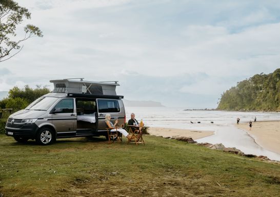 A couple sitting in front of a campervan overlooking Umina Beach, NRMA Ocean Beach Holiday Resort, Umina Beach